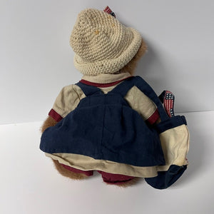 Vintage teddy bear wearing a knitted hat and overalls on a white background