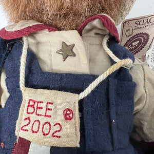 Close-up of a teddy bear with a vest and star emblem, featuring a label with 'BEE 2002' text.