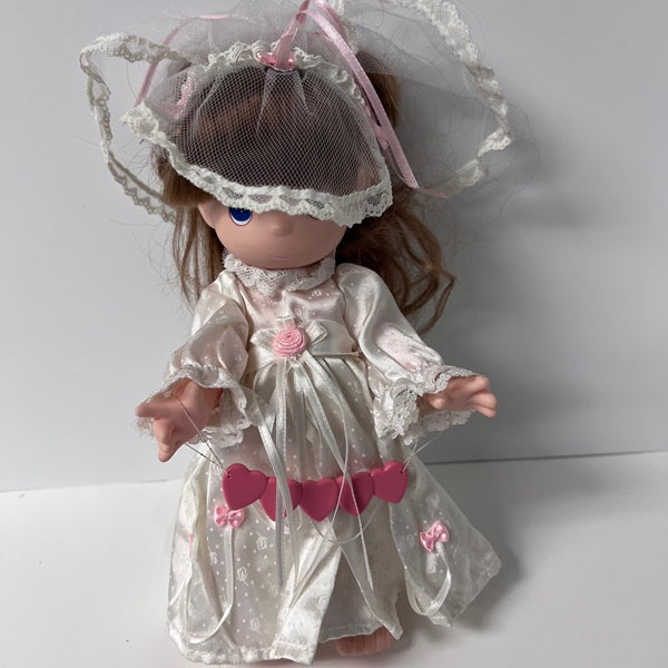 Doll in a white dress with lace details and pink hearts on a plain background