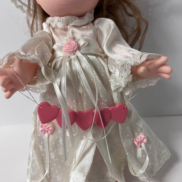 Doll wearing a white dress with pink floral details on a plain background