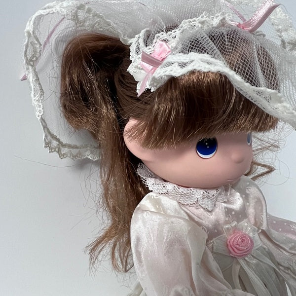 Close-up of a doll with brown hair, blue eyes, and a white lace headband on a light gray background.