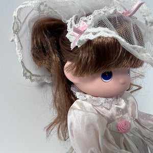 Close-up of a doll with brown hair, blue eyes, and a white lace headband on a light gray background.