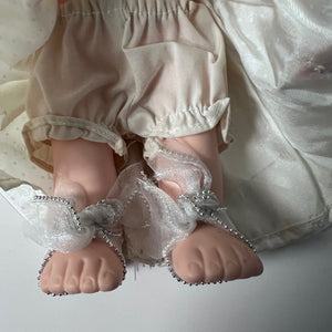 Close-up of doll feet wearing no shoes with decorative ribbons on a light background