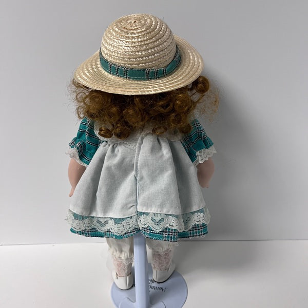 Doll wearing a straw hat and white dress with lace details on a white background