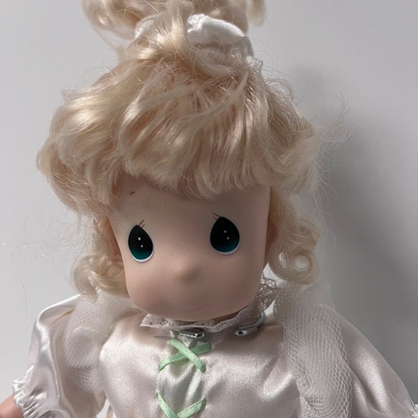 Close-up of a doll with blonde hair and green eyes wearing a white dress.
