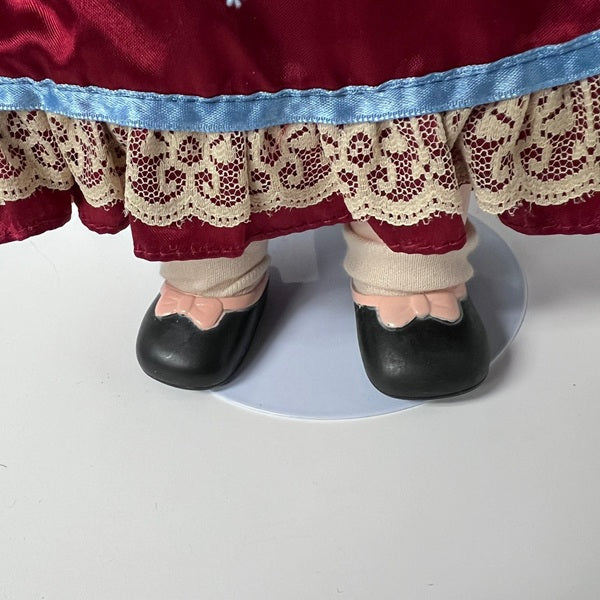 Close-up of a doll's feet wearing black shoes and beige stockings with a red skirt and blue lace trim.