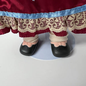 Close-up of a doll's feet wearing black shoes and beige stockings with a red skirt and blue lace trim.
