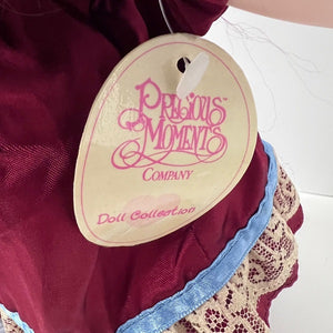 Close-up of a 'Precious Moments Company Doll Collection' tag on a maroon garment with lace details.