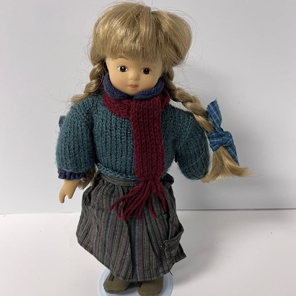 Doll wearing a blue sweater, red scarf, and plaid skirt on a white background