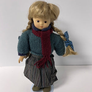 Doll wearing a blue sweater, red scarf, and plaid skirt on a white background