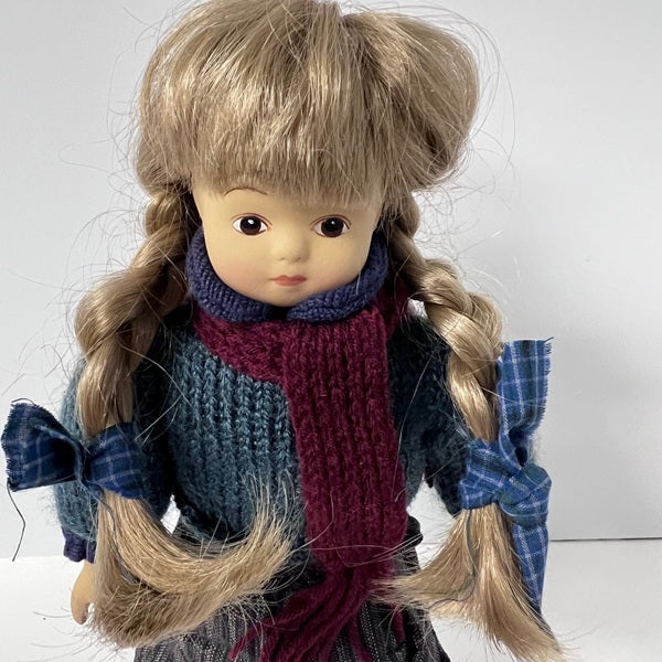Doll with blonde hair styled in pigtails, wearing a blue outfit and red scarf on a white background