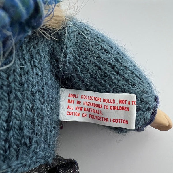 Close-up of a doll with a label on its arm, set against a white background.