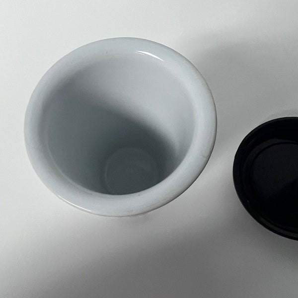 White ceramic cup with a black lid on a light gray background