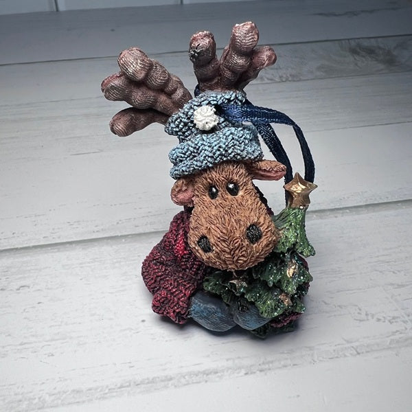 Decorative figurine of a moose wearing a knitted hat and scarf on a wooden surface