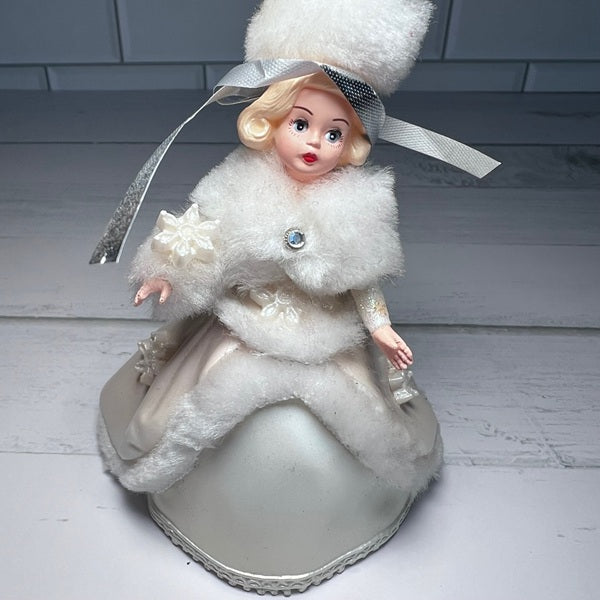 Vintage-style doll in a white fur coat and hat on a wooden surface