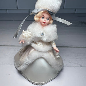 Vintage-style doll in a white fur coat and hat on a wooden surface