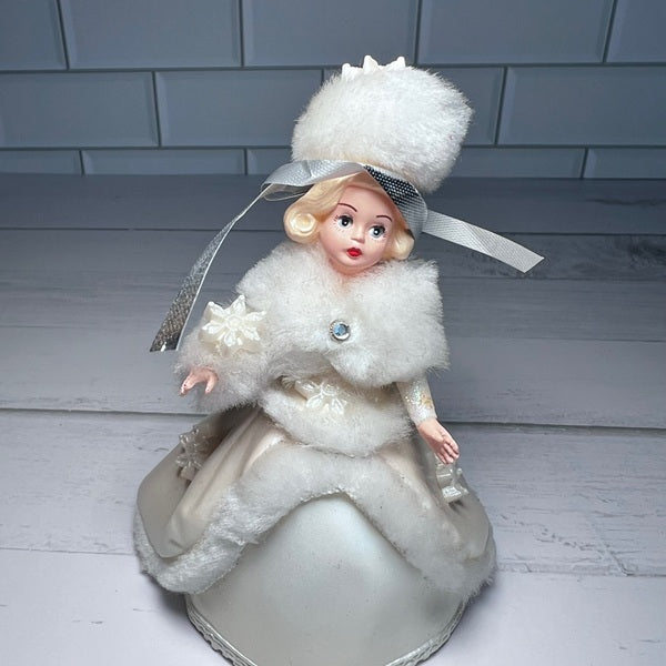 Vintage-style doll in a white fur coat and hat on a wooden floor.