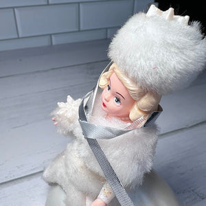Vintage doll with blonde hair and white fur outfit on a light wooden floor.