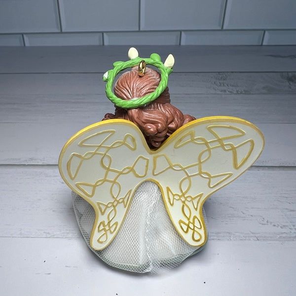 Decorative head with angel wings and green hairband on a light wooden surface