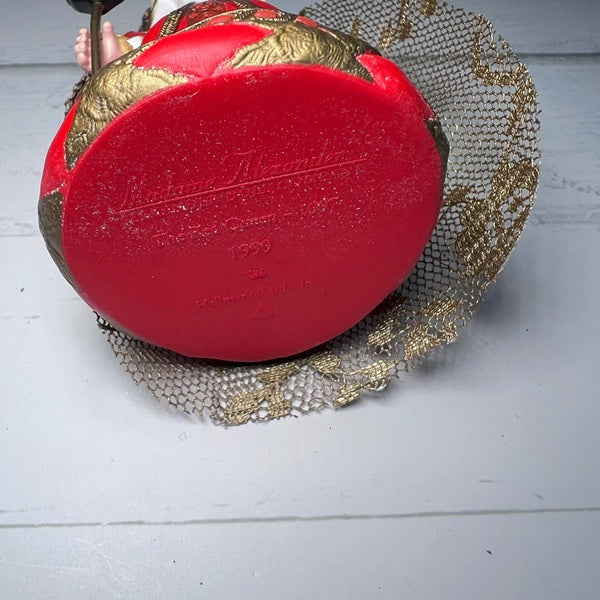 Red and gold decorative item with a brand logo on a light wooden surface
