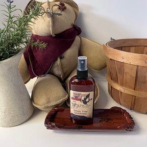 Bottle of body spray unscented on a wooden tray with a teddy bear, plant, and basket in the background.