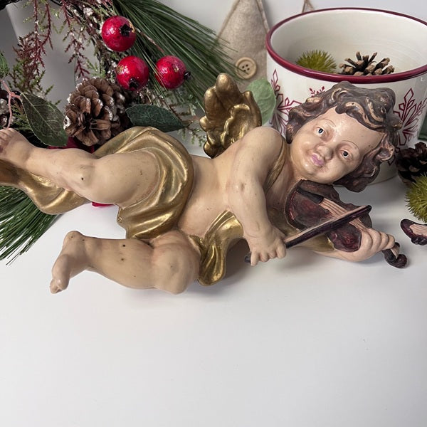Statue of a cherub playing a violin with Christmas decorations in the background