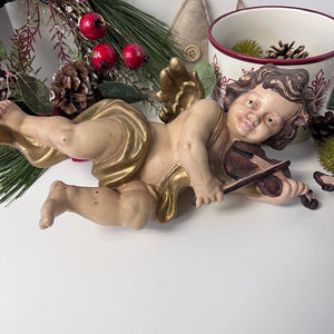 Statue of a cherub playing a violin with Christmas decorations in the background