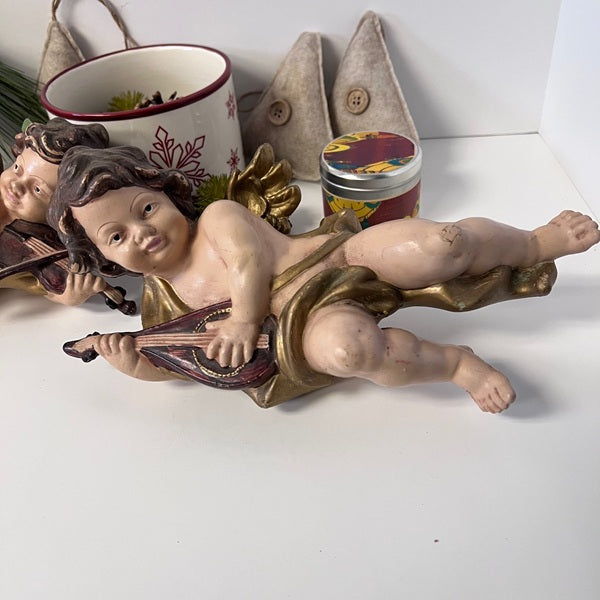 Decorative figurine of a child playing a lyre on a white surface with other decorative items.