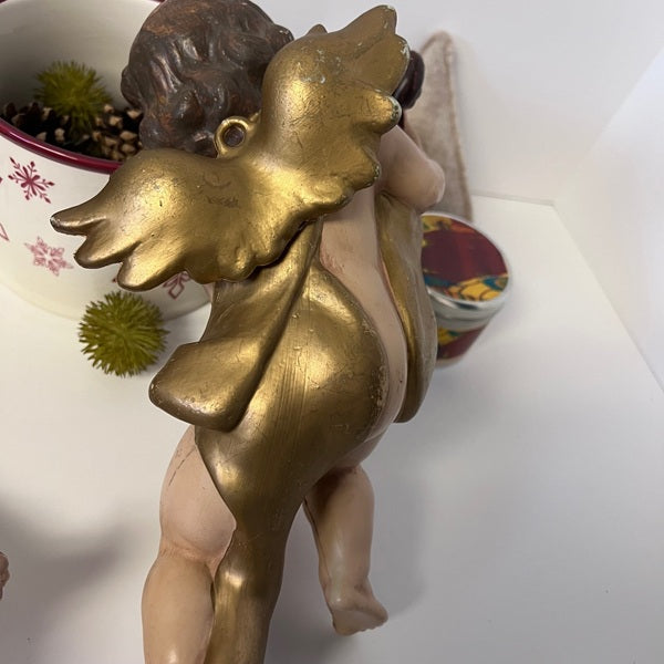 Gold angel figurine on a white surface with decorative items in the background