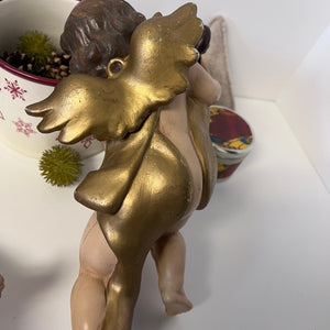 Gold angel figurine on a white surface with decorative items in the background