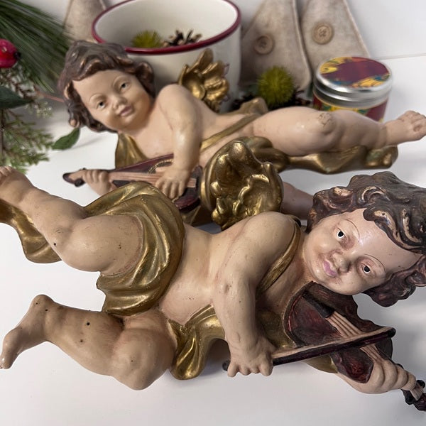 Decorative cherub figurines with gold accents on a white surface.