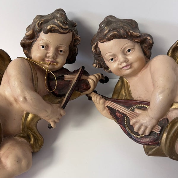 Two cherubic figures playing musical instruments on a white background