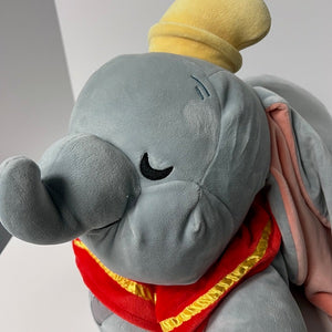 Plush toy elephant with a yellow hat and red outfit on a plain background