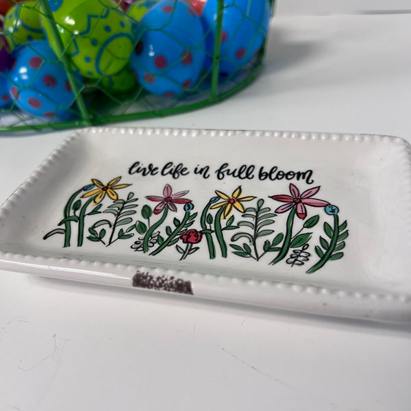 Decorative tray with floral design and 'live life in full bloom' text, placed on a white surface with colorful Easter eggs in the background.