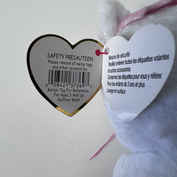 Heart-shaped safety precaution tag on a plush toy with text in multiple languages.