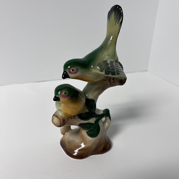 Two ceramic birds on a branch against a white background