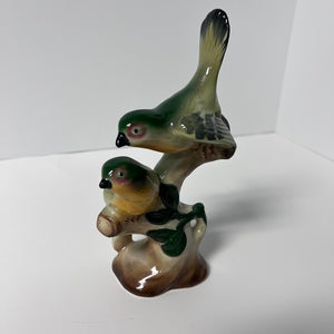 Two ceramic birds on a branch against a white background