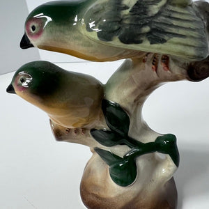 Ceramic sculpture of two birds perched on a branch with leaves.