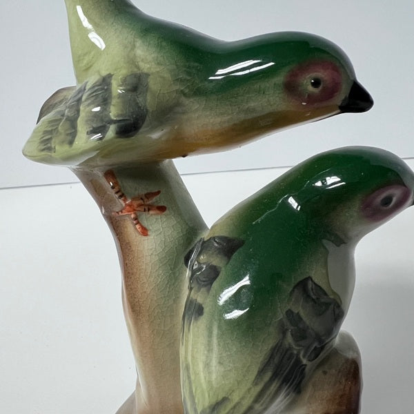 Two ceramic birds on a branch against a white background