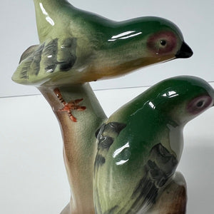 Two ceramic birds on a branch against a white background