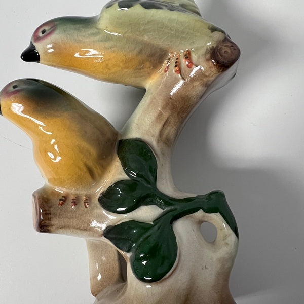 Ceramic sculpture of two birds perched on a branch with leaves.