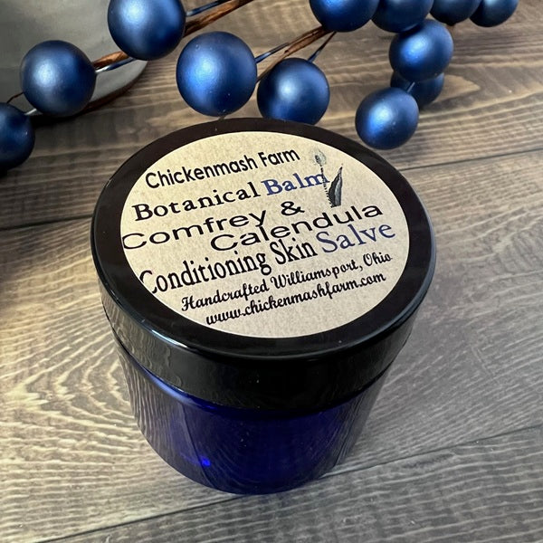 Blue jar of Chickenmash Farm Botanical Balm with a label on a wooden surface.