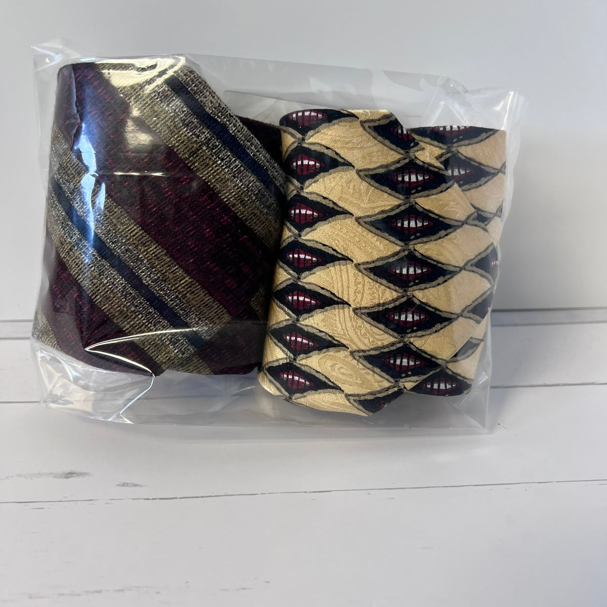 Two patterned ties in a clear plastic bag on a white surface