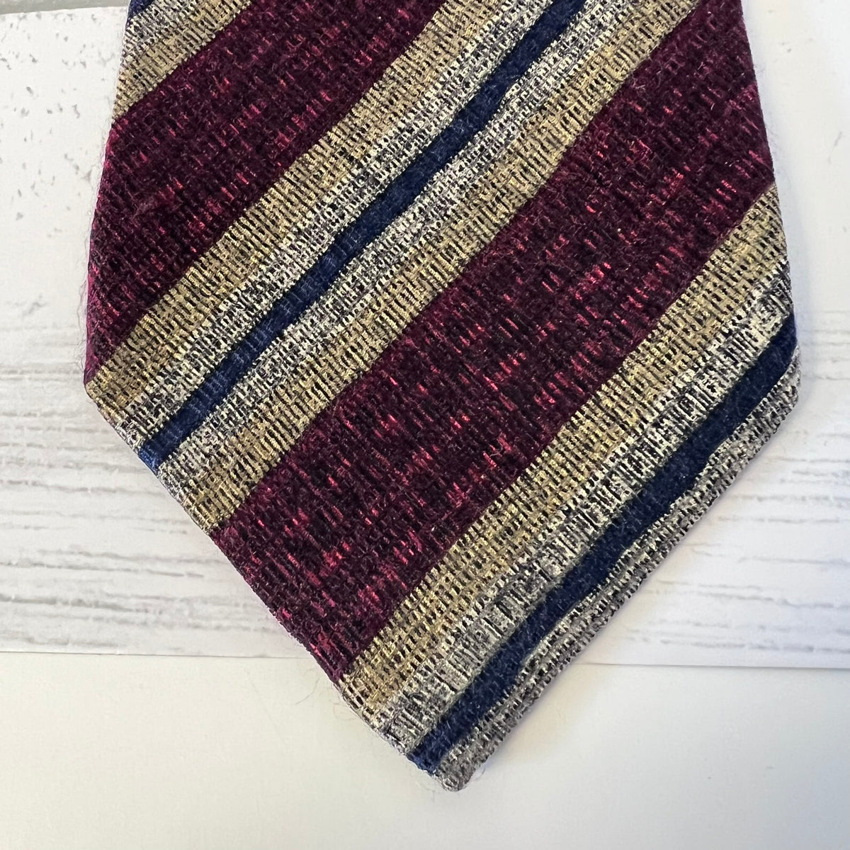 Striped tie with maroon, beige, and navy pattern on a white surface