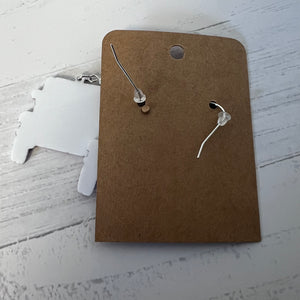 Silver earrings on a brown cardboard backing with a white surface underneath