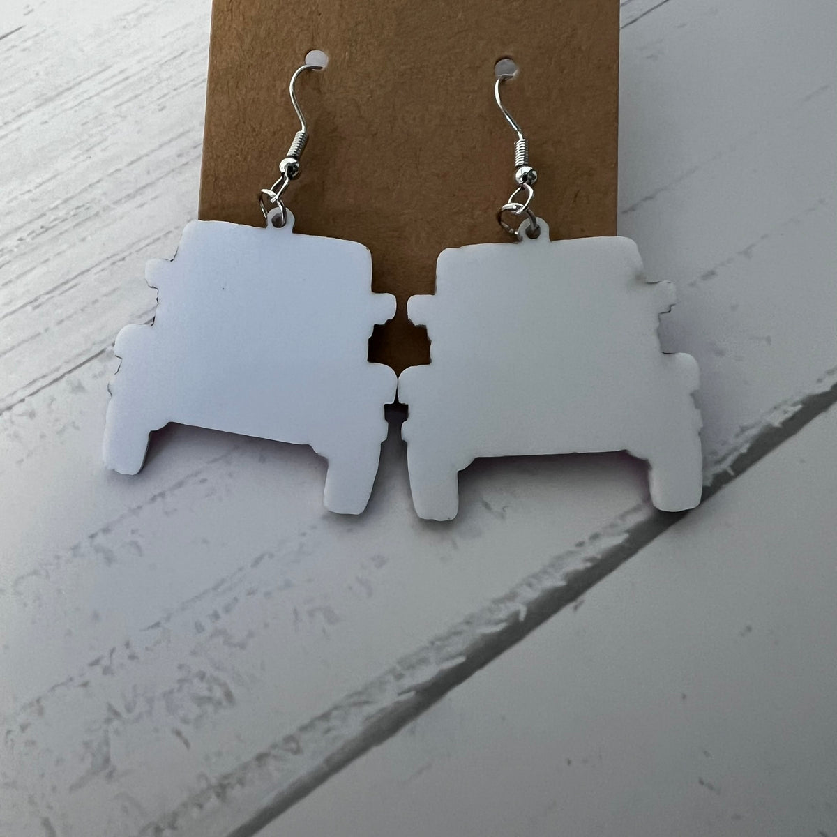 White puzzle piece earrings on a brown card against a white background