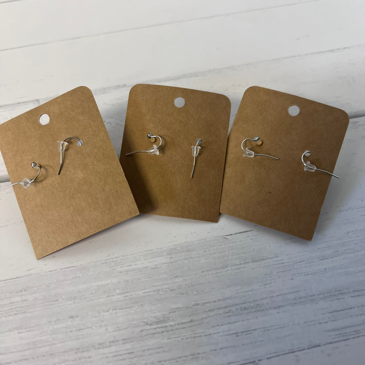 Four pairs of earrings on brown card stock against a white wooden background