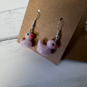 Purple duck-shaped earrings on a brown card with a white background