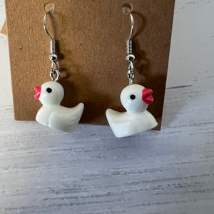 White duck-shaped earrings with red beaks on a brown card against a gray background