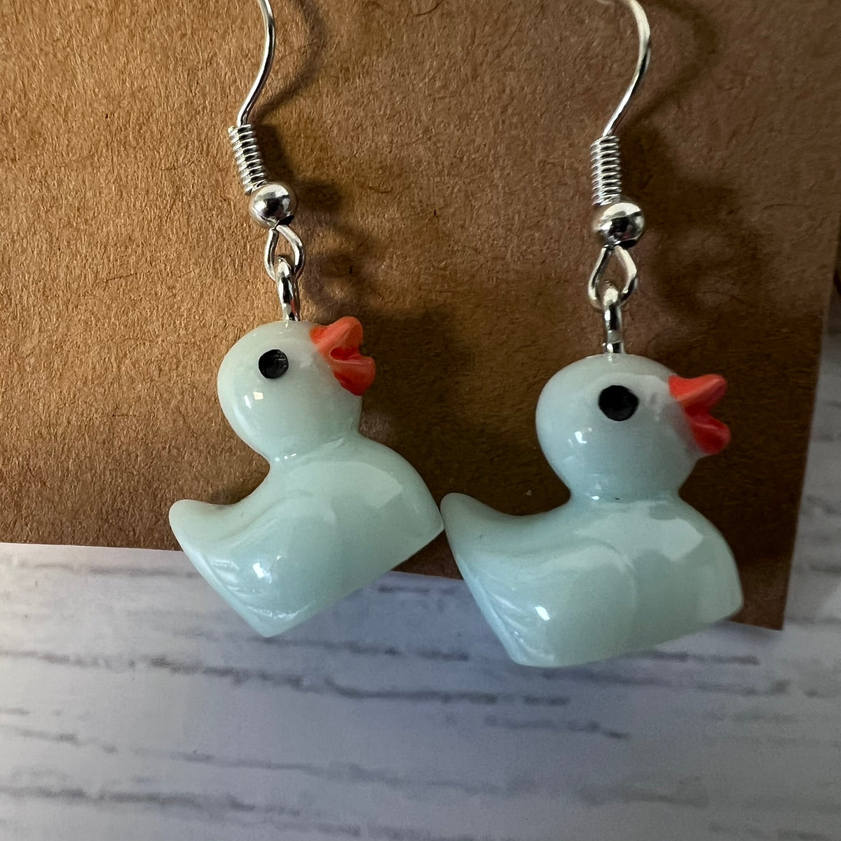 Pair of duck-shaped earrings on a marble surface with a brown background